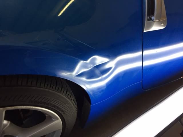Blue car with a dent in the rear quarter panel, near the tire.