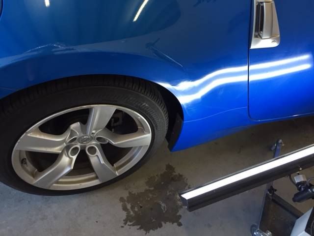 Blue car with a dent in the side. A wheel and tire are visible, as well as some tools.
