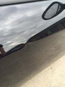 Black car's side with a dent, reflecting a cloudy sky and an outside mirror.