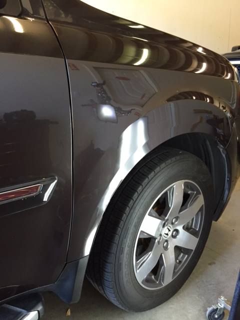 Brown car's front quarter panel, showing reflections of a garage, wheel, and tire.