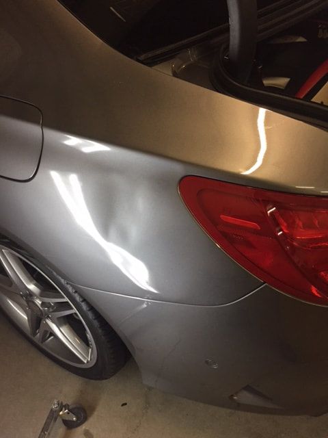 Gray car rear quarter panel with dent near taillight, wheel visible.