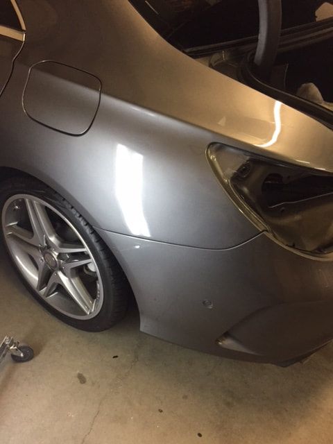 Gray car's rear quarter panel with dent, taillight removed, and wheel visible, indoors.
