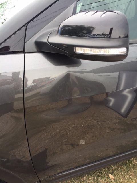 Gray car with a dent on the driver's side door, side mirror visible.