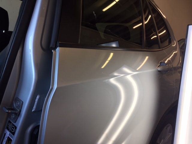 Silver car door with a dent, inside a well-lit garage or shop.