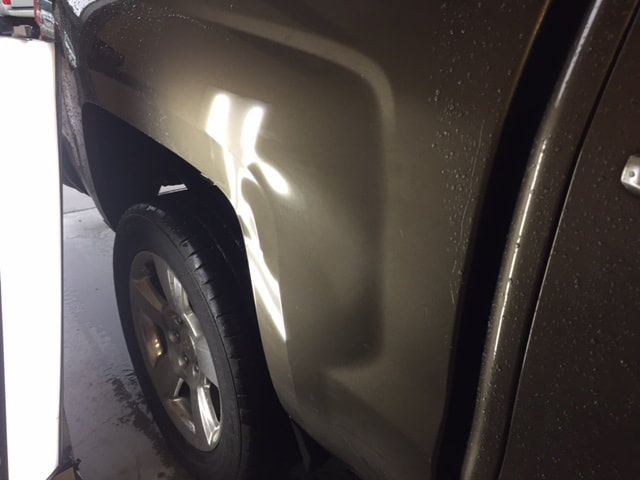 A brown pickup truck's side panel with a dent, reflecting light.