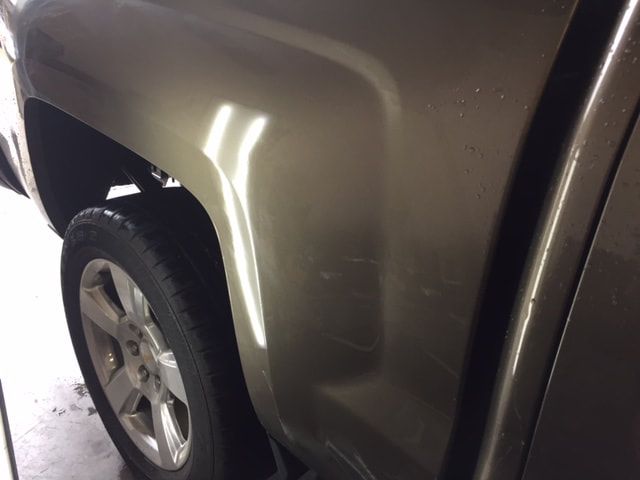 A dented, metallic-colored truck bed near the wheel, reflecting overhead lights.
