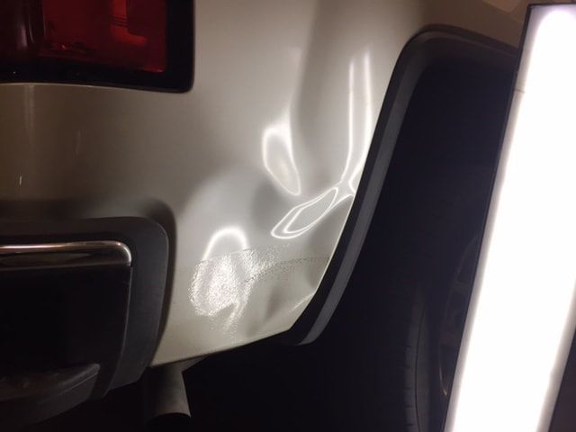 White car panel with multiple dents, near a black bumper.