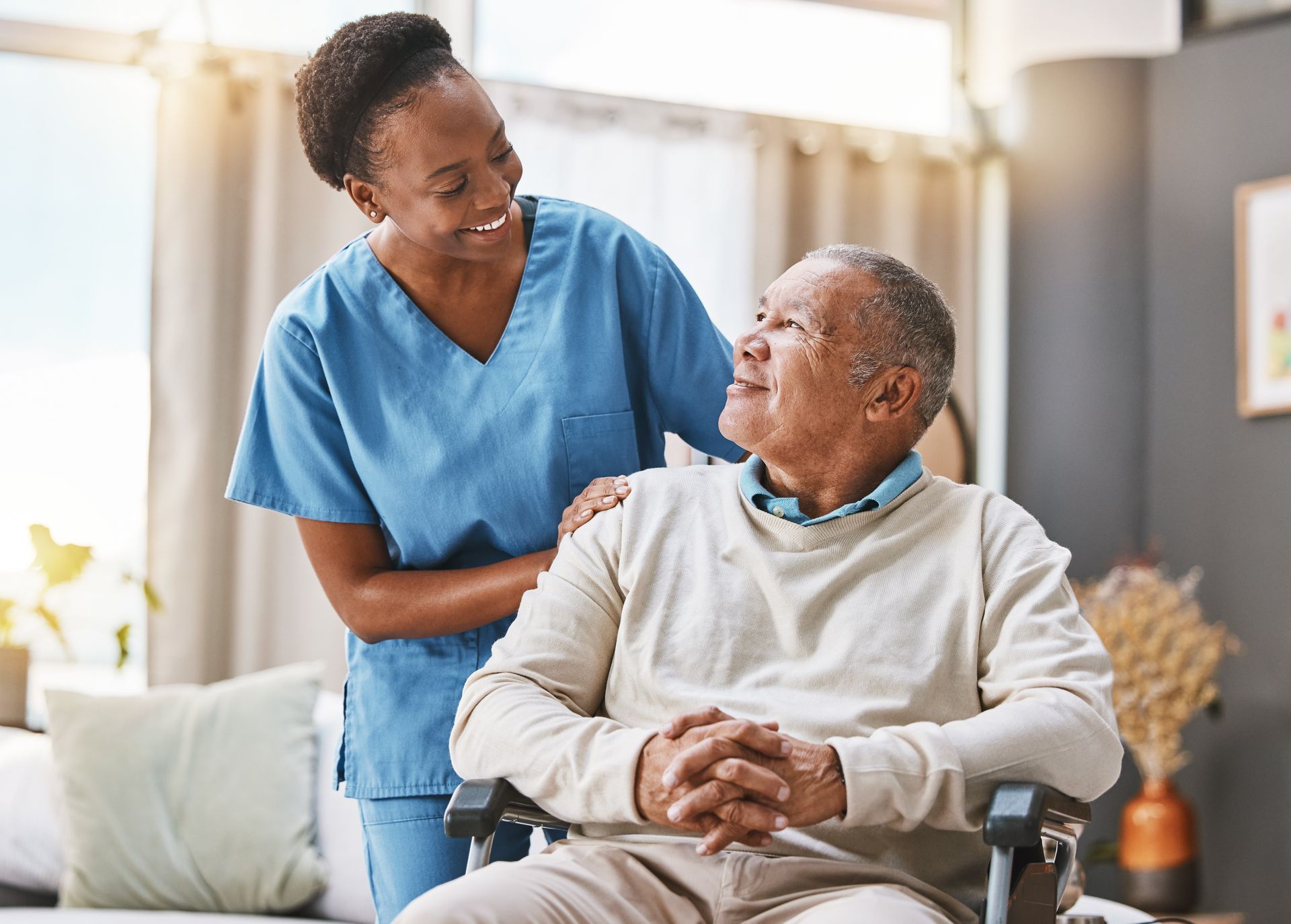 A caregiver supporting an elderly man in a wheelchair at his home.