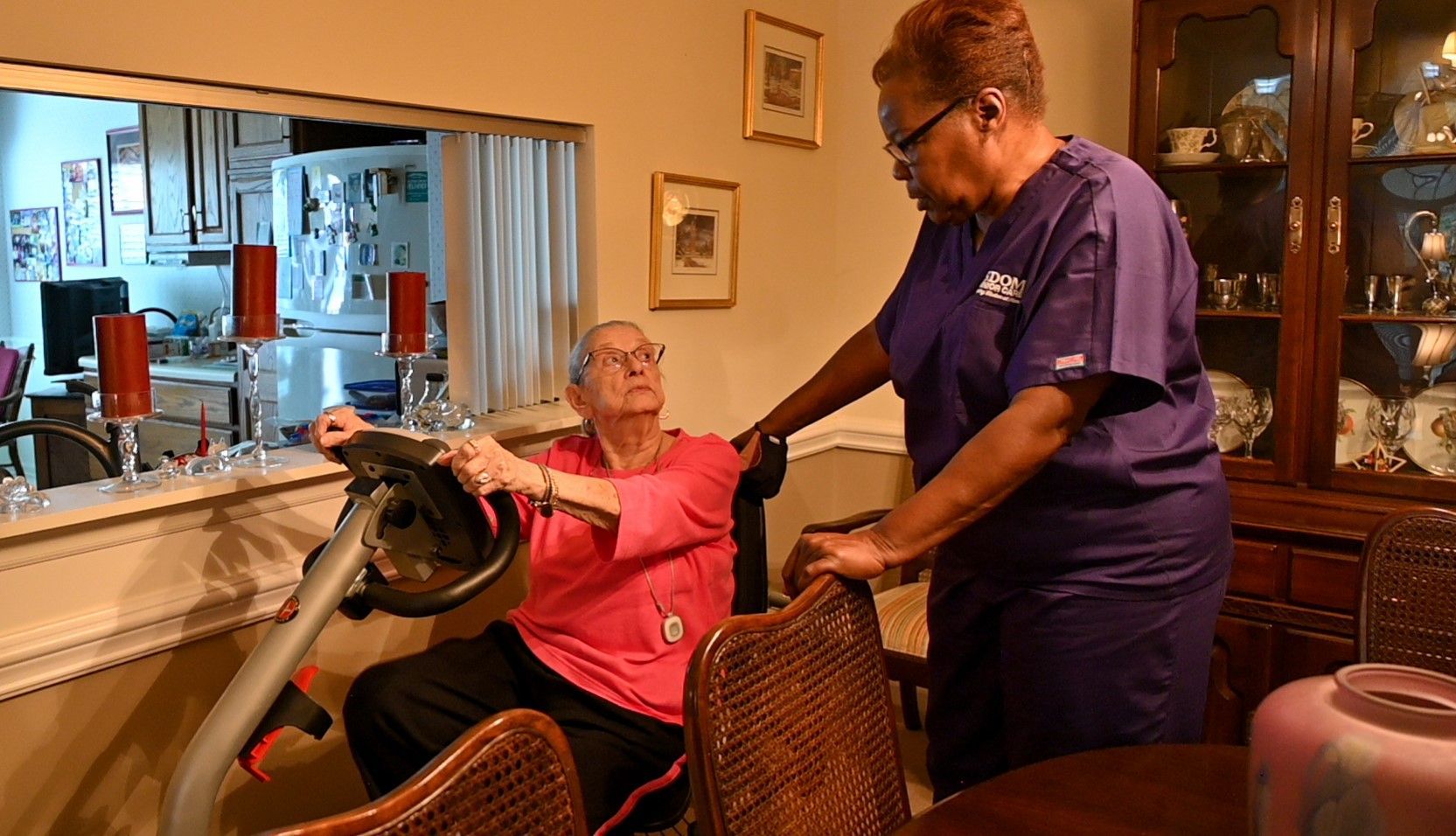 Caregiver assists a person using an exercise bike indoors.