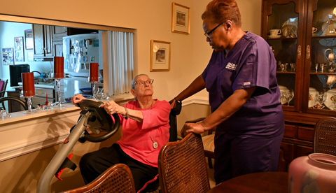 Caregiver assists a person using an exercise bike indoors.