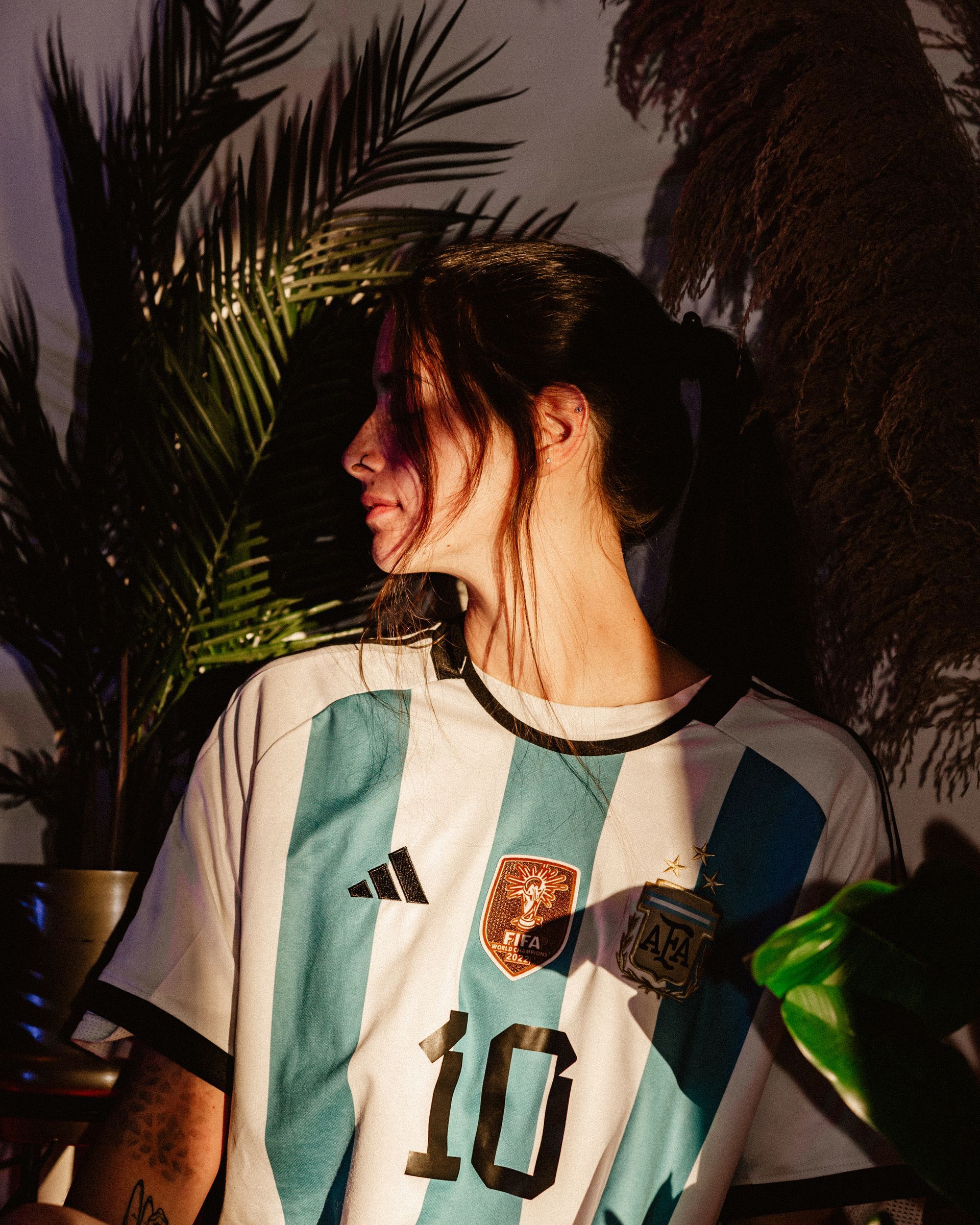 Person wearing an Argentina soccer jersey, standing near plants.