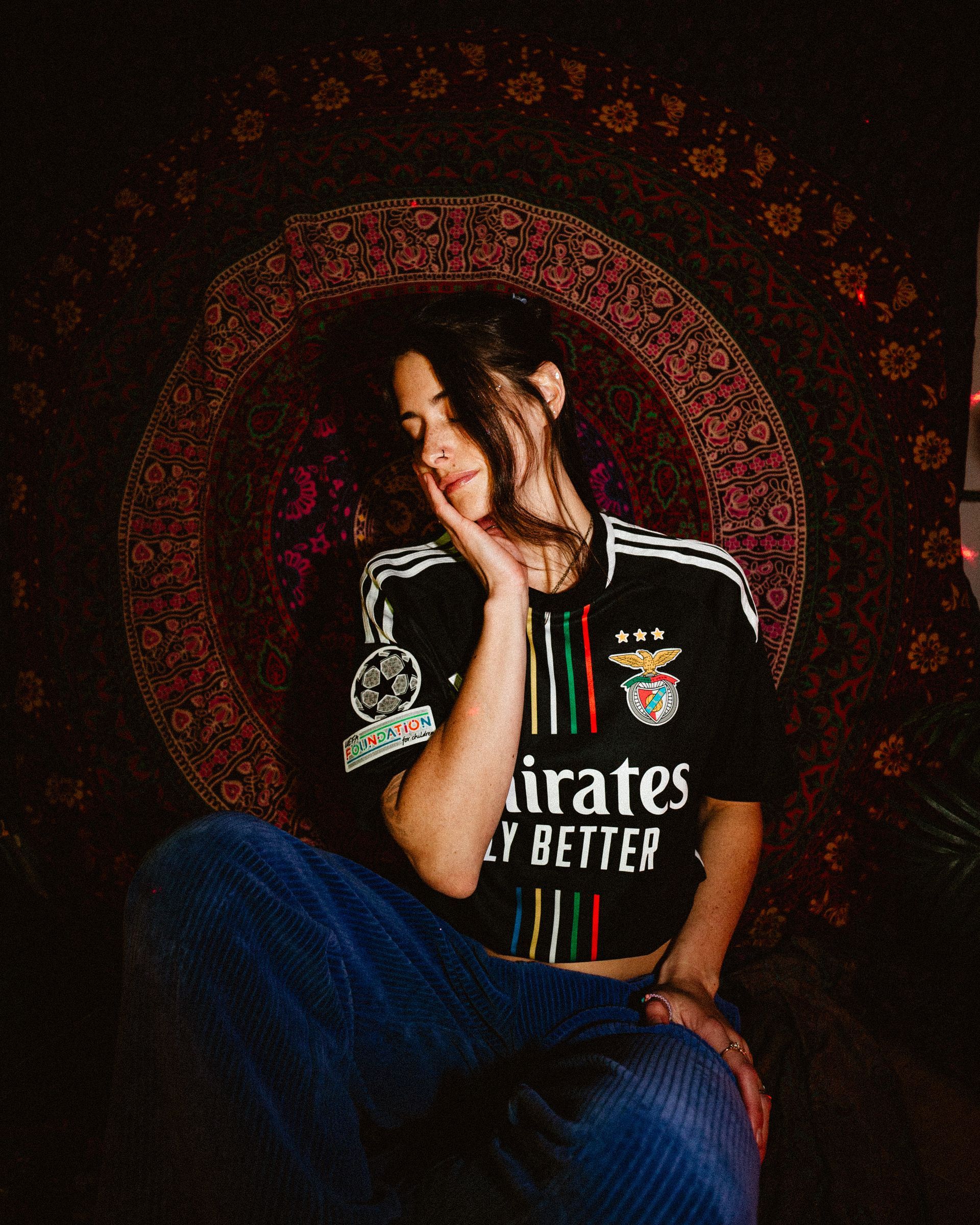 Woman in soccer jersey sits, hand on face, in front of a tapestry.