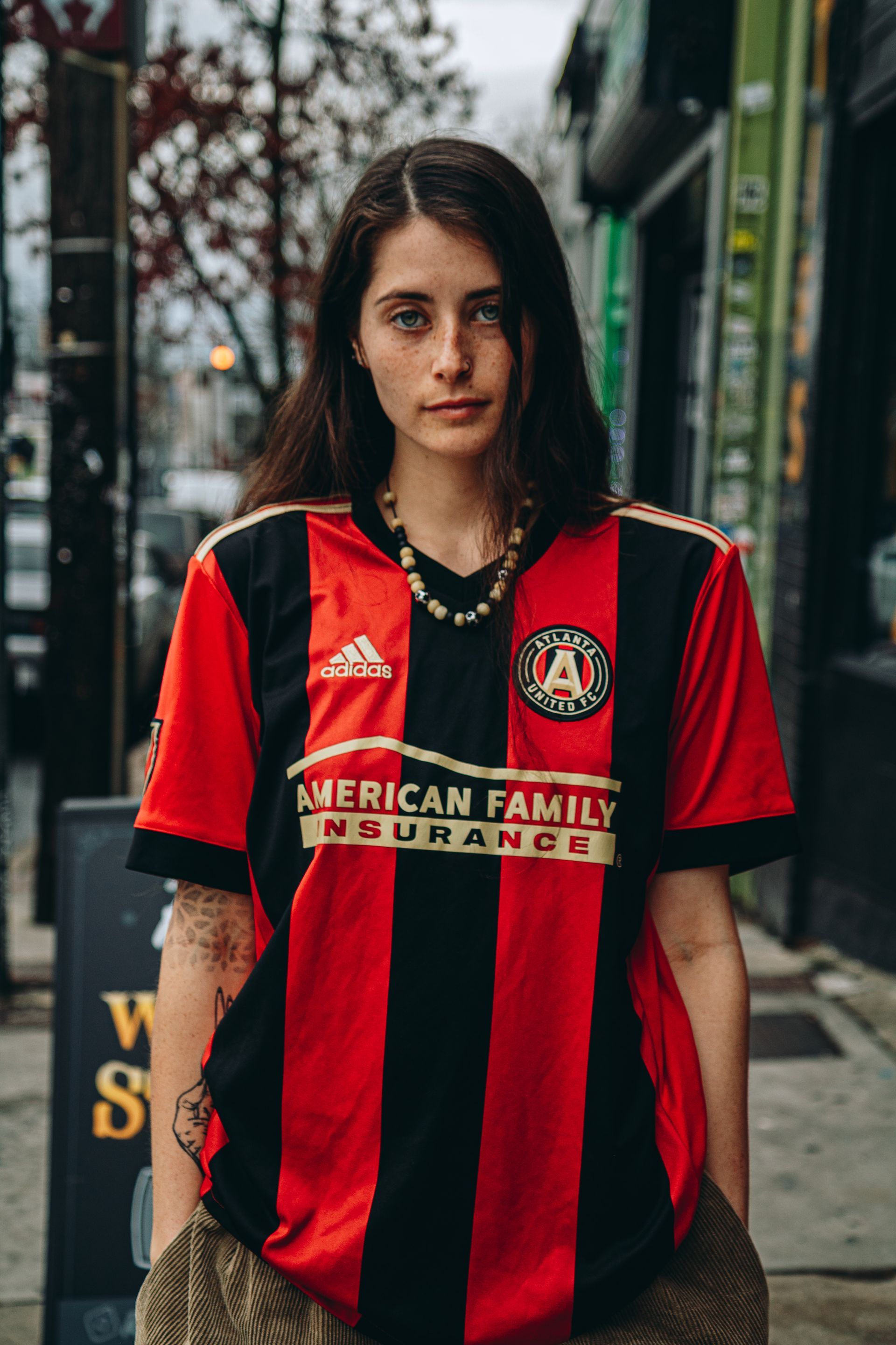 Woman in red and black soccer jersey stands outside.