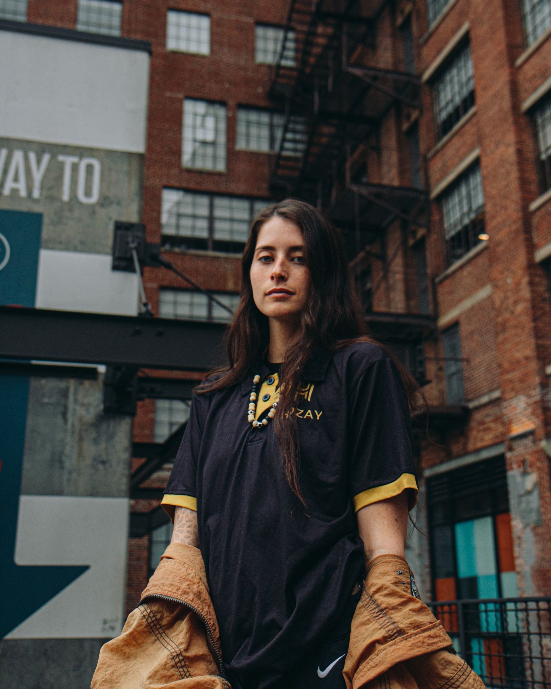 Woman in black shirt with yellow trim in front of brick building.