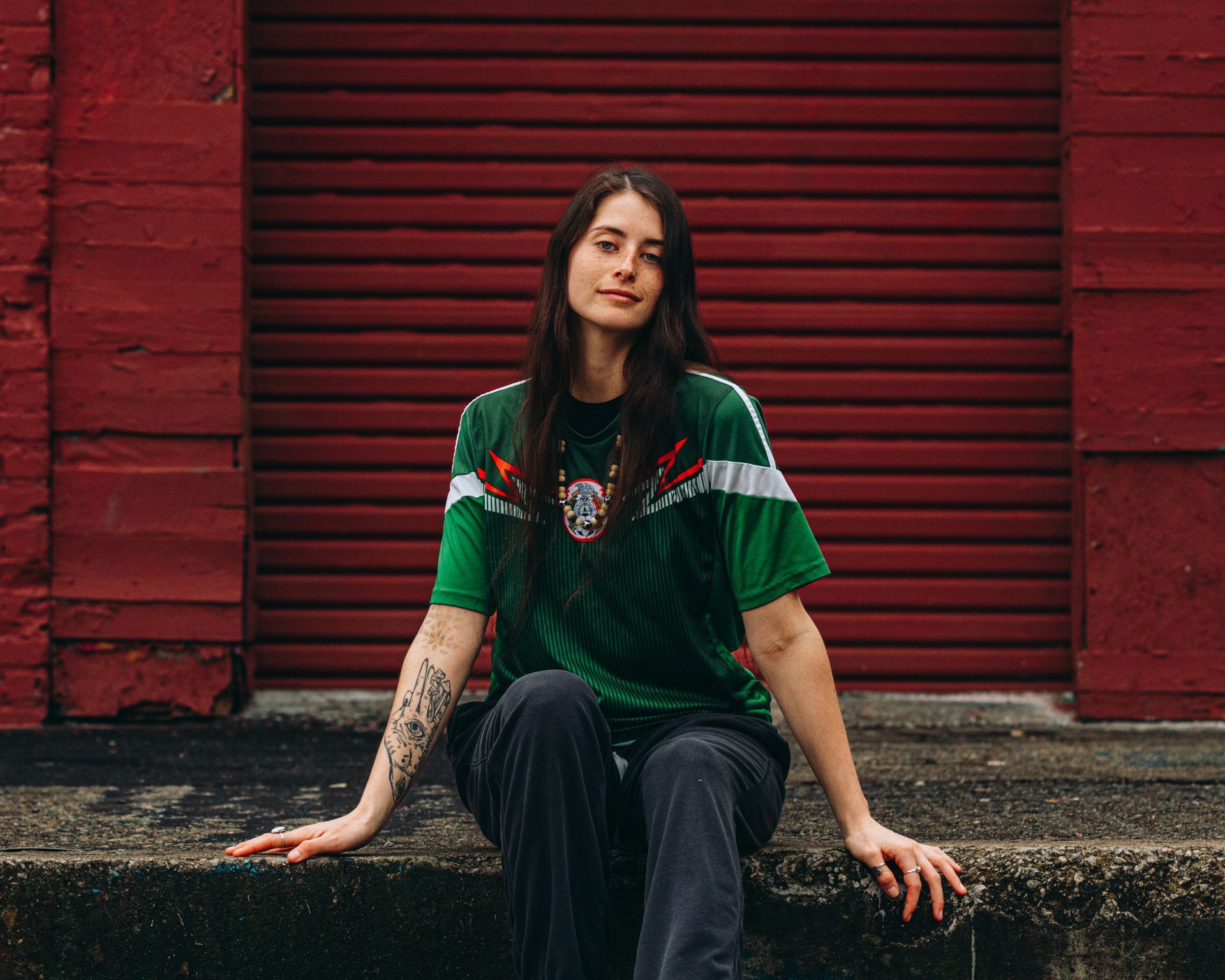 Person wearing a green jersey sits on steps in front of a red wall.