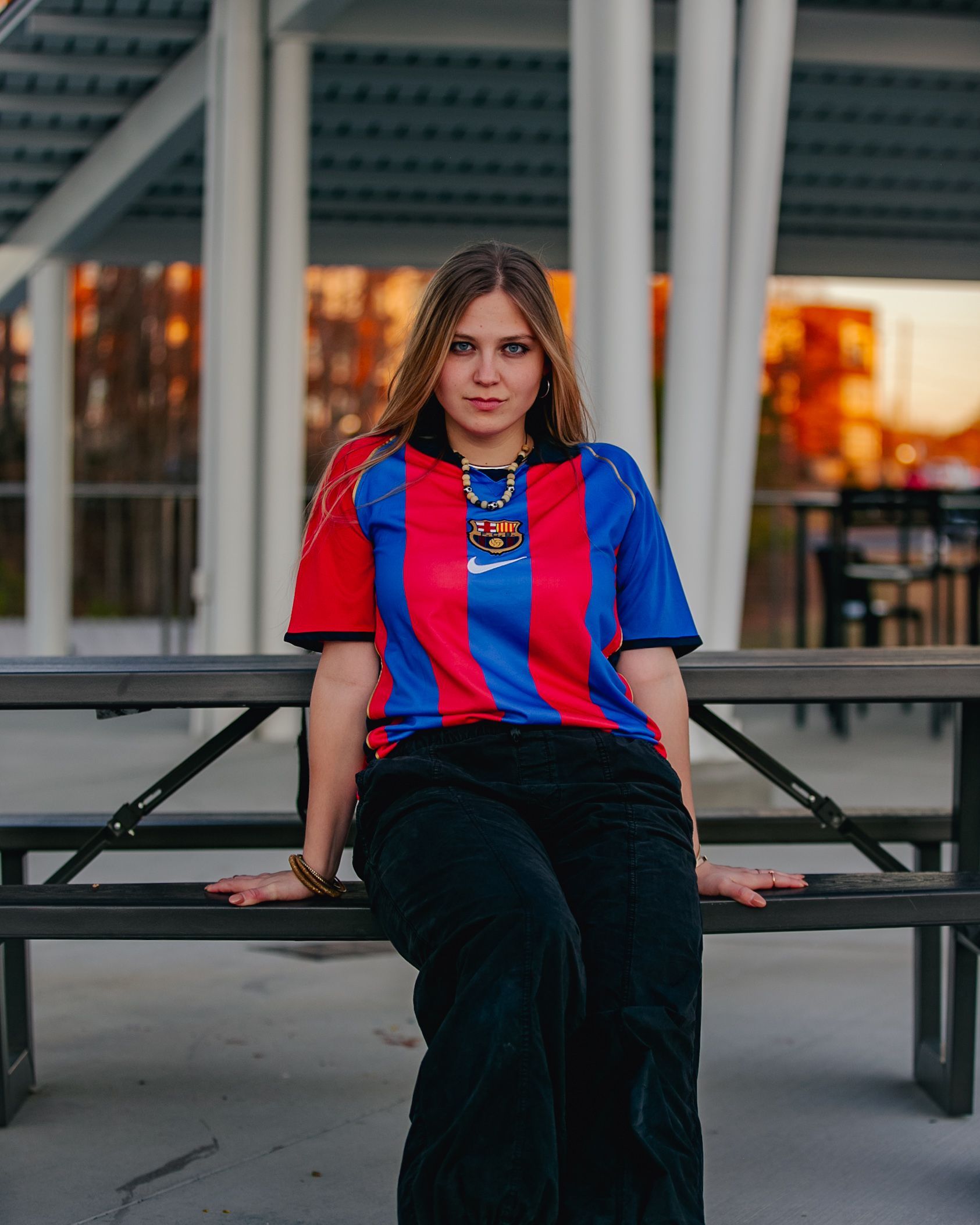 Woman wearing a Barcelona jersey and black pants, sitting on a park bench.