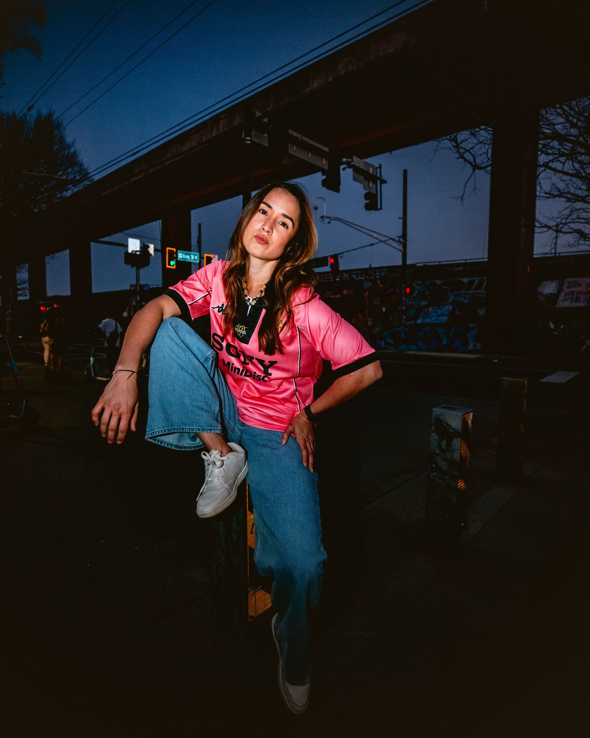Woman in pink shirt and jeans, sitting outside at night.
