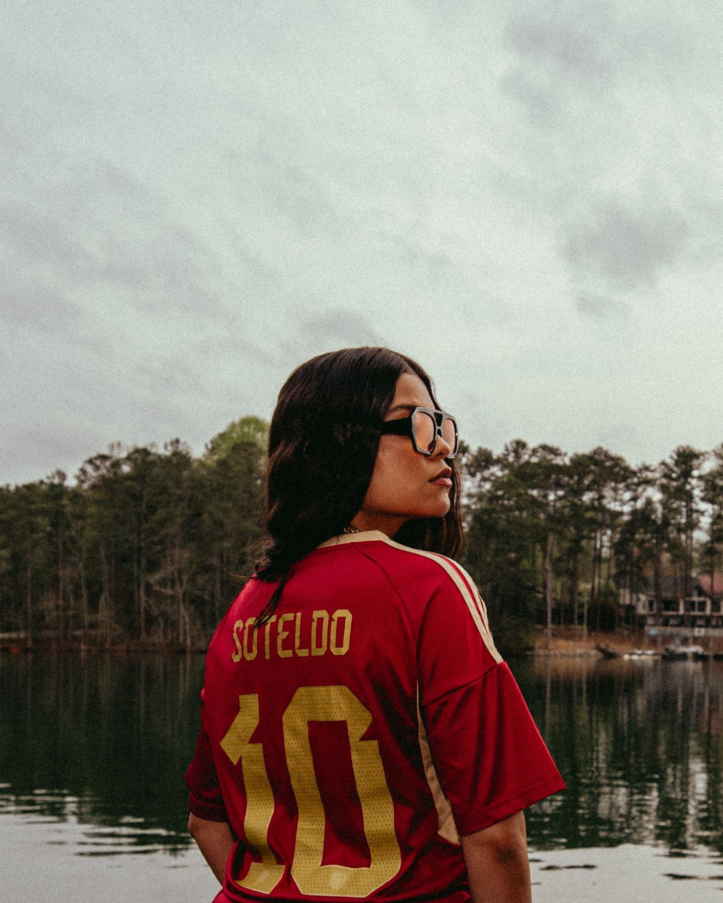Woman wearing glasses and a red soccer jersey with the number 10, standing by a lake.