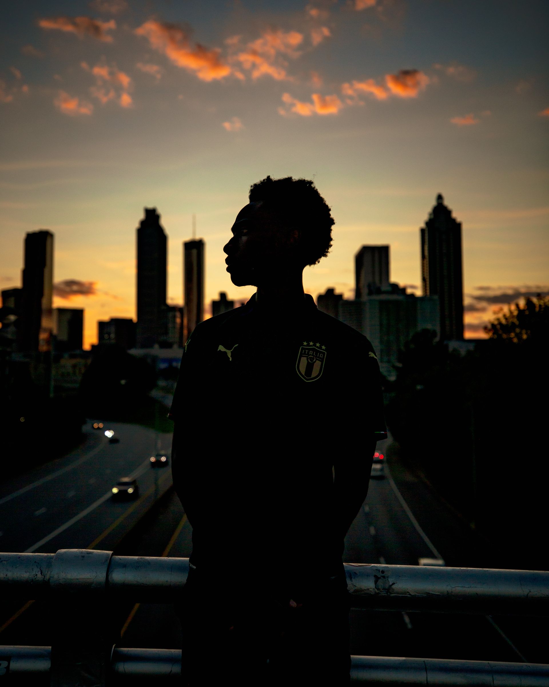 Silhouette of person looking at city skyline during sunset.