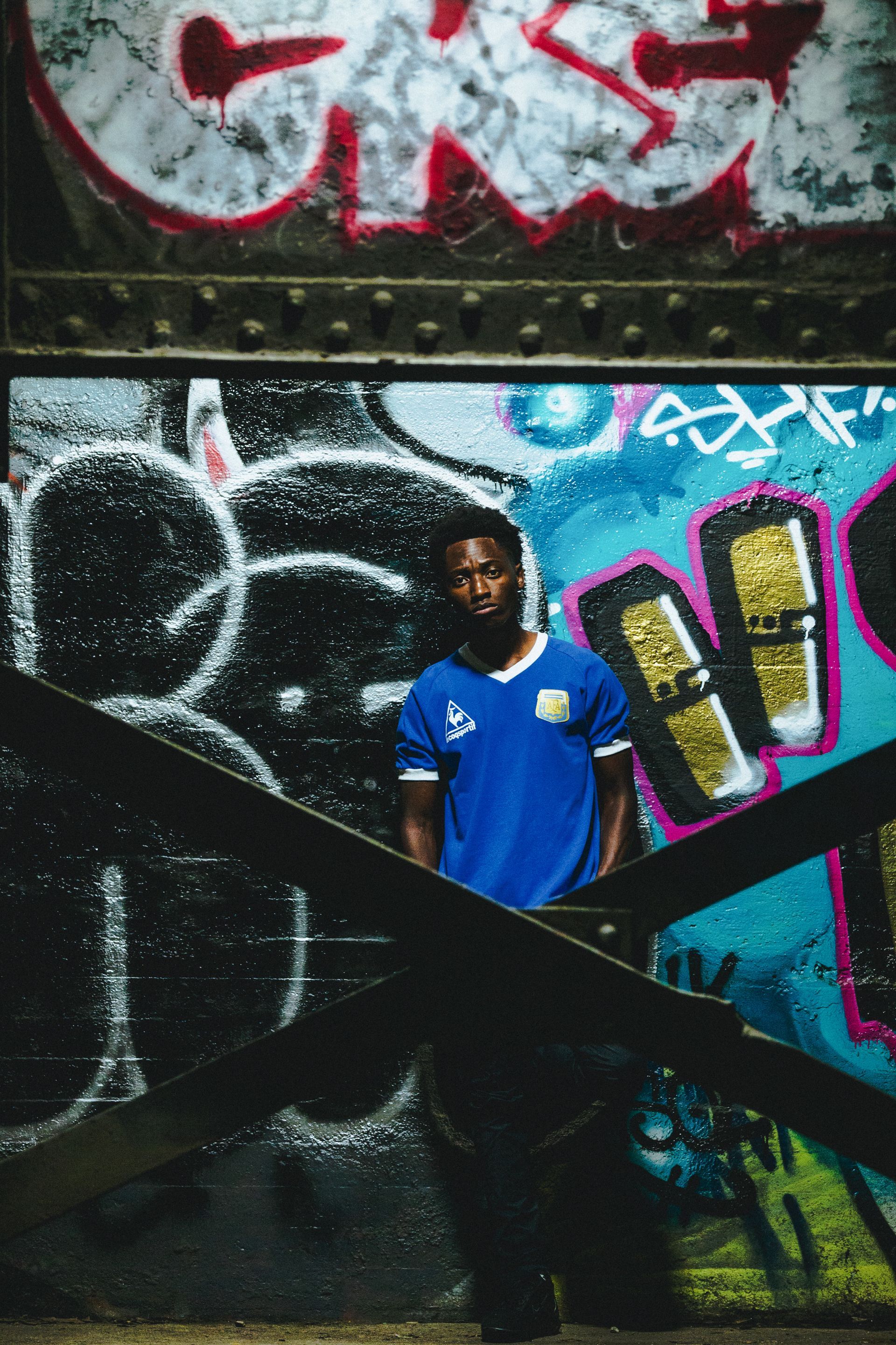 Man in blue shirt stands near graffiti-covered wall, framed by wooden beams.