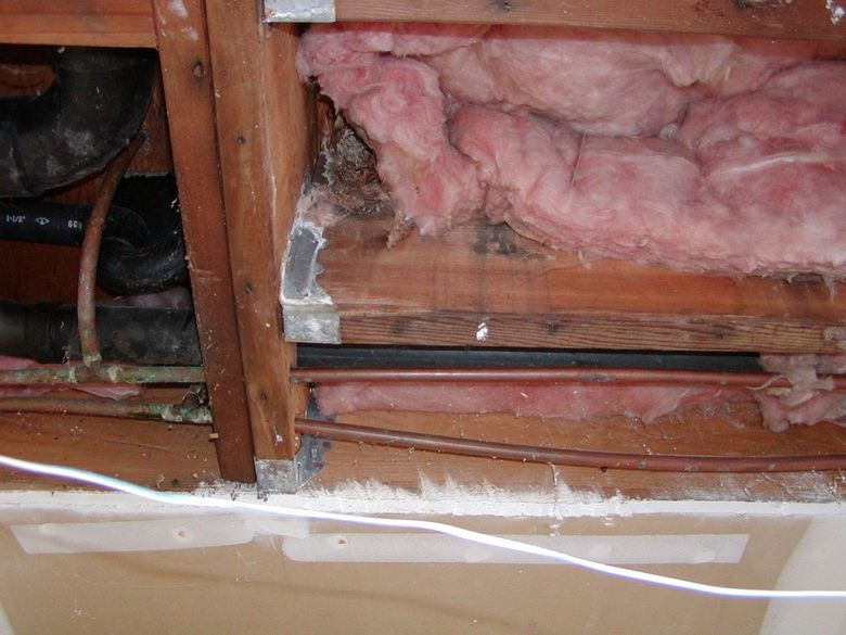 A ceiling with pink insulation and pipes coming out of it