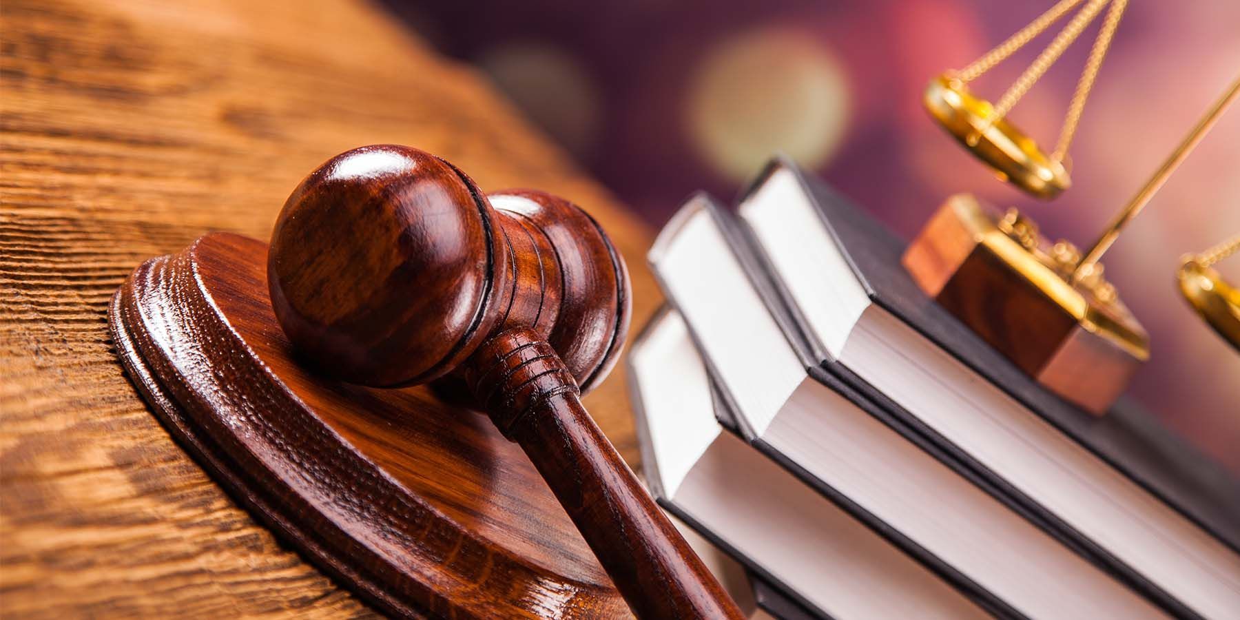 A wooden gavel is sitting on top of a wooden table next to a stack of books and a scale of justice.