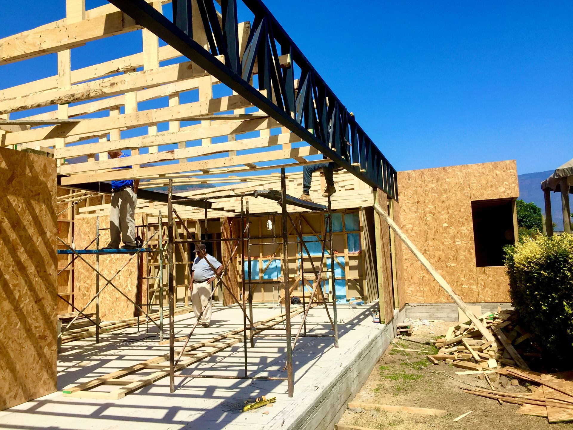 Sitio de construcción con estructura de madera, una viga de acero negra y una persona caminando.
