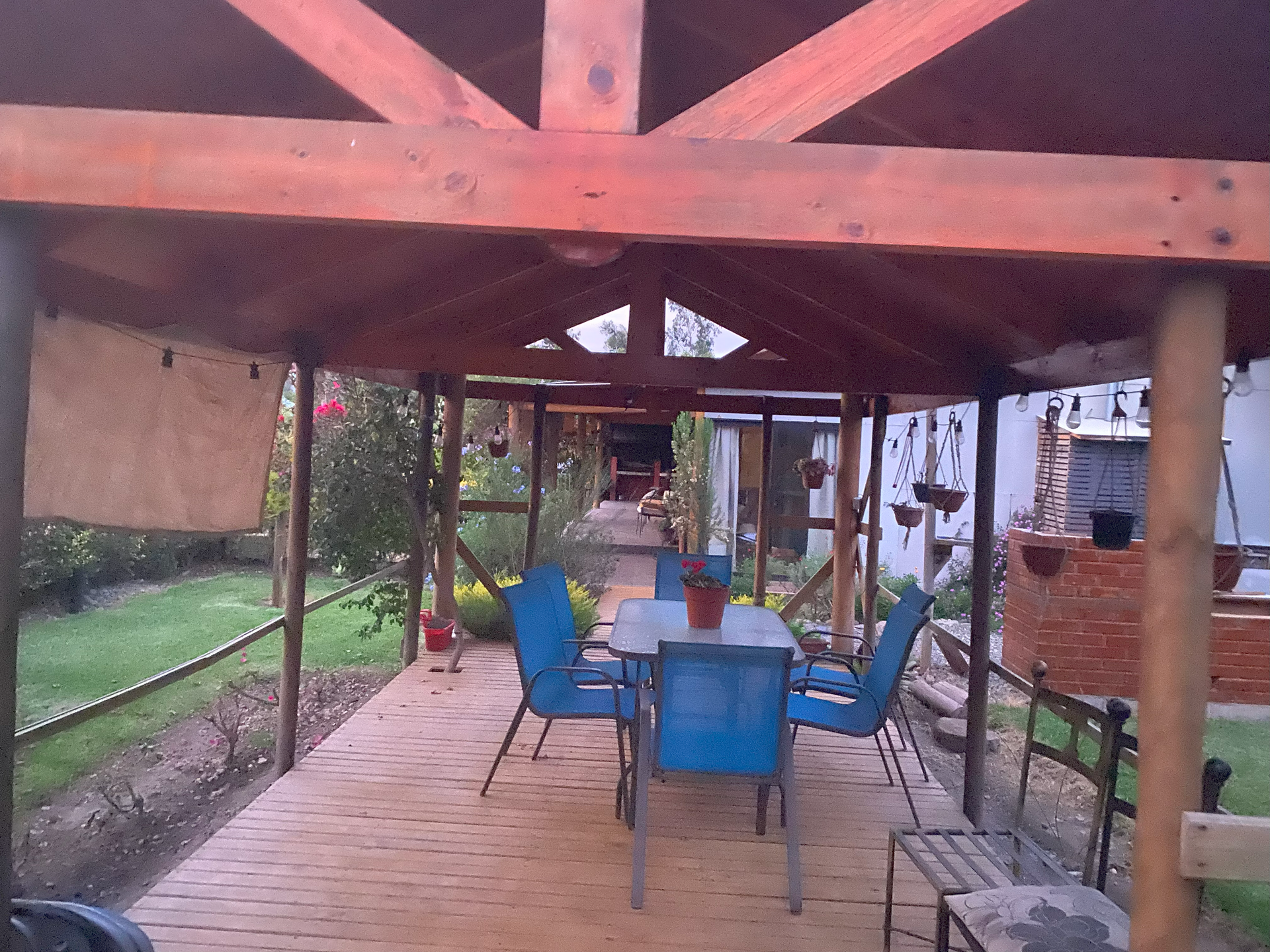 Cenador de madera al aire libre con mesa de comedor y sillas azules, en un entorno de jardín.
