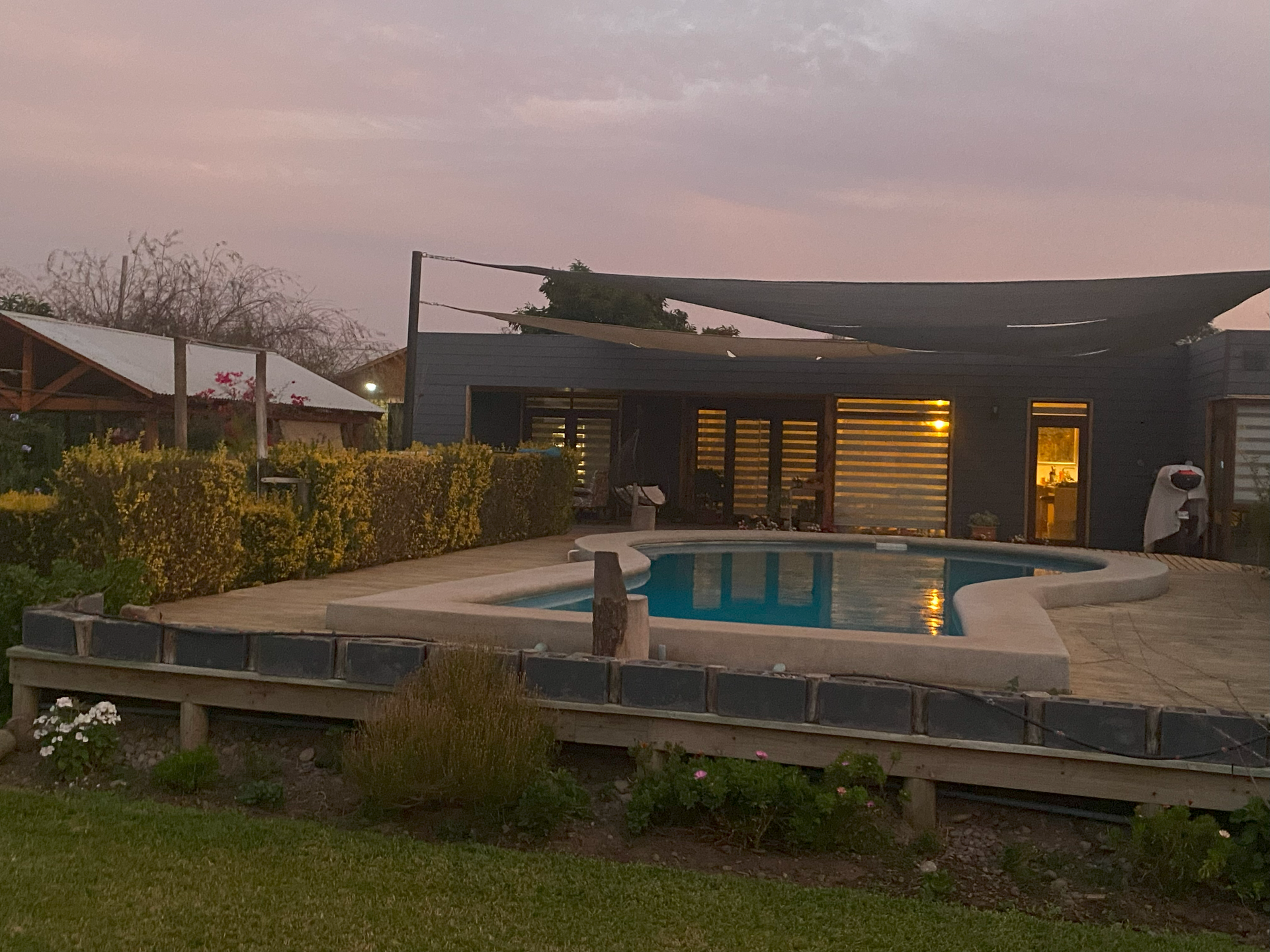 Una casa moderna con piscina al anochecer, con un cielo rosa y naranja.