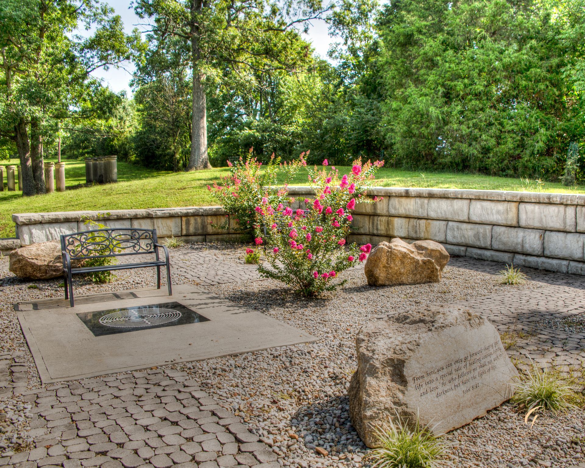 A brick wall with a bench and flowers in the background