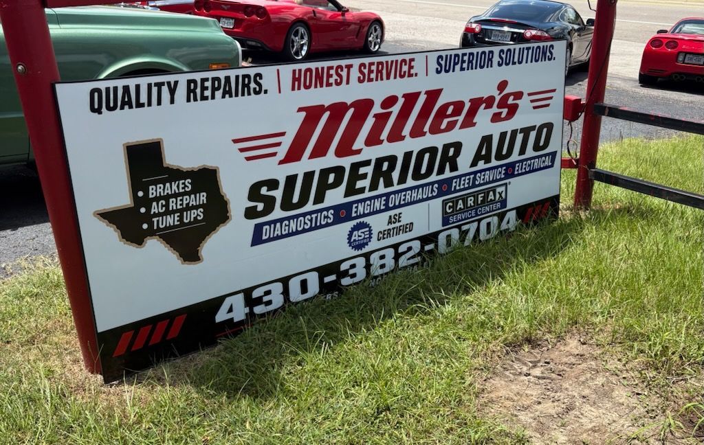 Miller’s Superior Auto roadside sign on grass, red truck in background, with services and phone number displayed