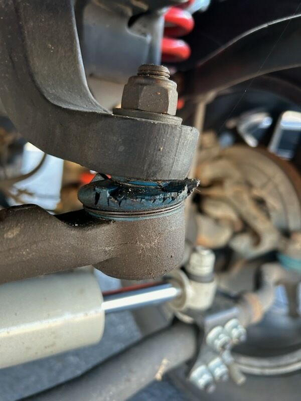 Close-up of a car suspension ball joint with a torn blue rubber boot and exposed grease.