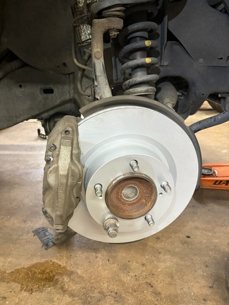 Car wheel hub and silver brake rotor with caliper, shown in a car wheel well.