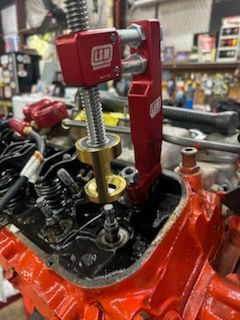 Red engine block with valve spring compressor tool installed in a workshop