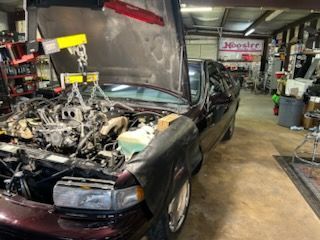Black sports car in a garage with its engine exposed during repair