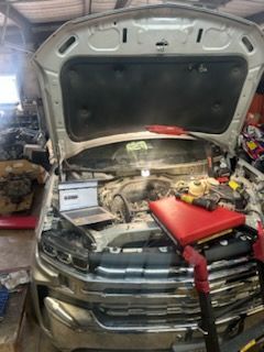 SUV with hood open in a garage, showing engine bay and red diagnostic equipment on the front.