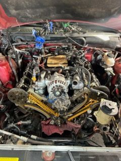 Car engine bay with exposed components and yellow timing chain under an open hood