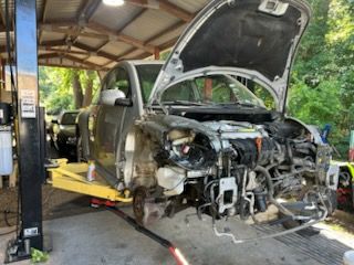 Damaged gray pickup truck on a lift in a garage, front end removed and hood open