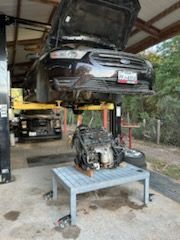 Car on a lift in a garage with its engine removed and placed on a table underneath.