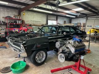 Black classic car in a garage with a large engine on a red stand in front
