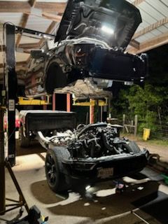 Car lifted on a hydraulic rack above a stripped black convertible in a garage at night