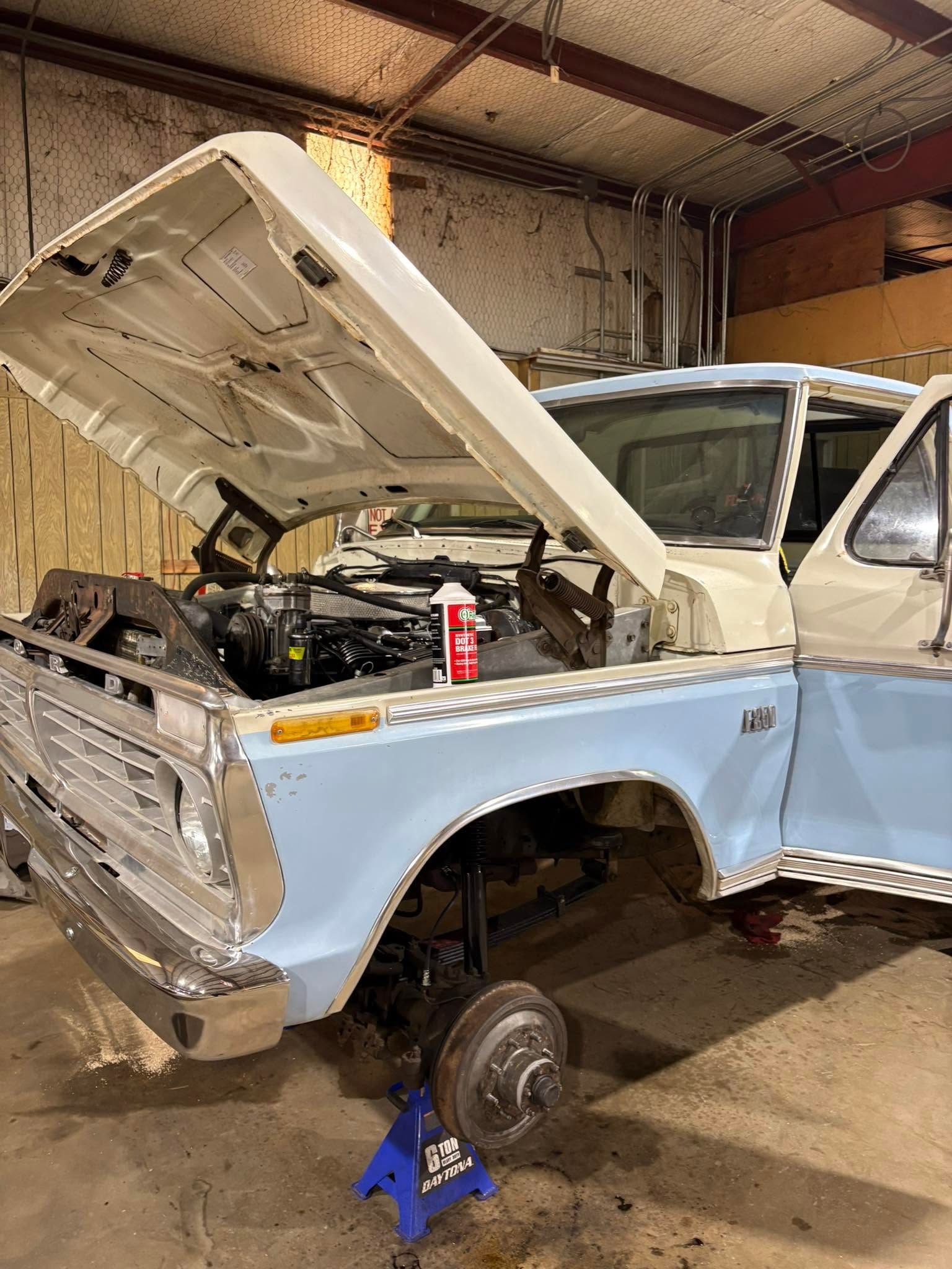Light blue vintage car with hood open in a garage, front wheel removed and engine exposed.