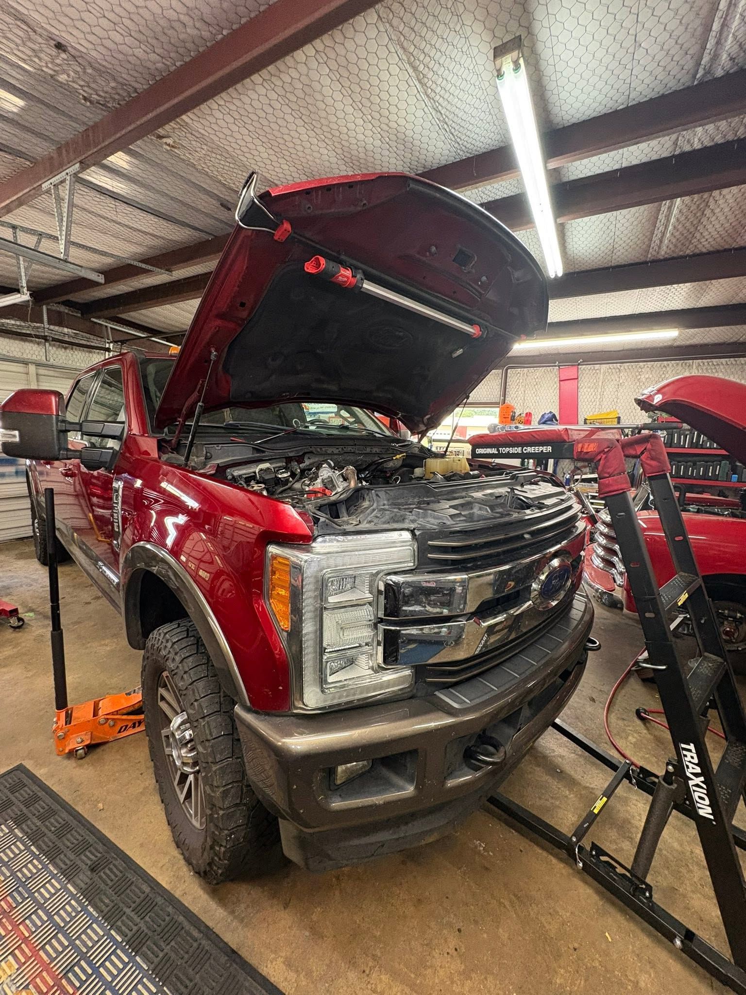 Red pickup truck with hood open in an auto repair shop, engine exposed and front bumper removed