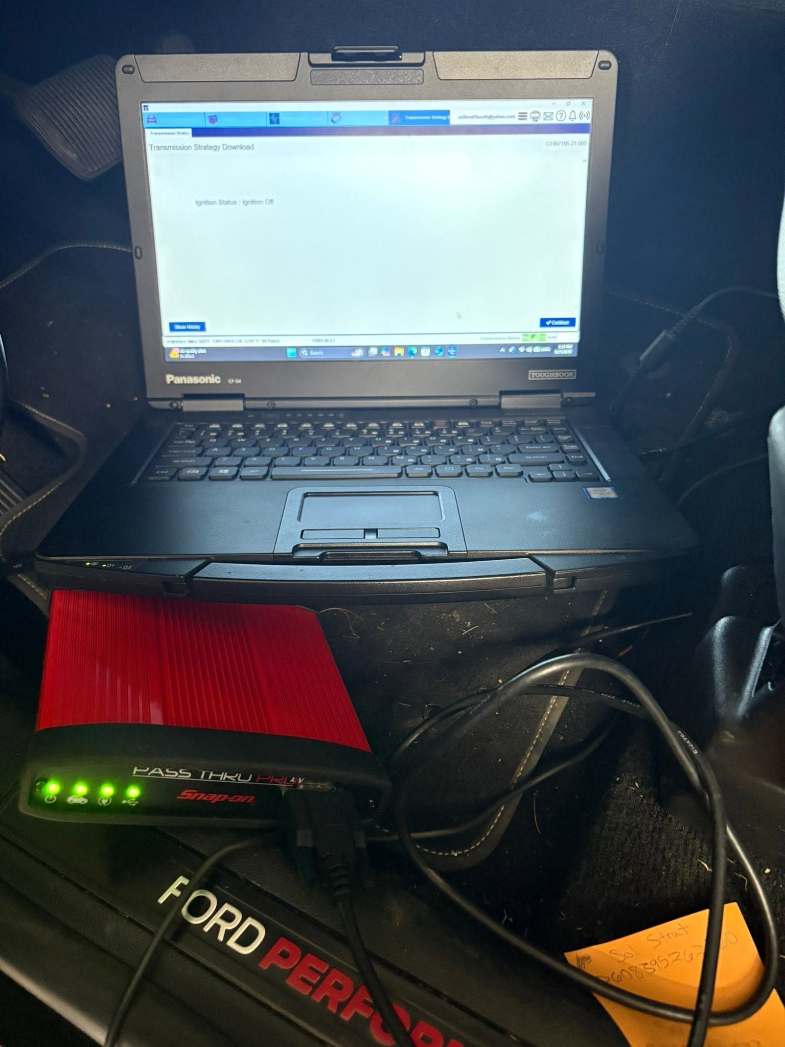 A rugged laptop on a car seat, showing a mostly blank screen with a red cloth and Ford-branded item in front.