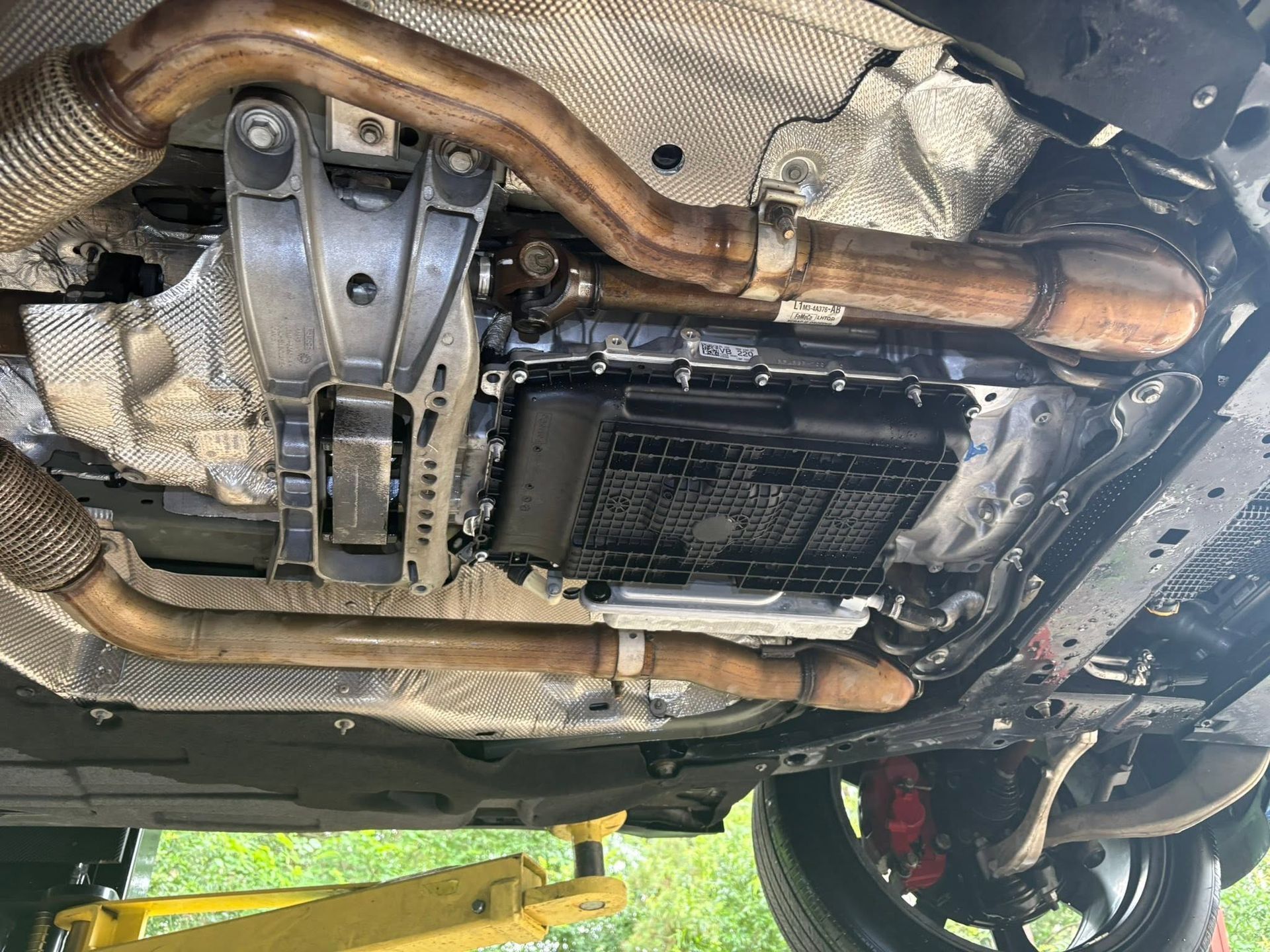 Undercarriage of a car on a lift, showing exhaust pipes, heat shielding, and engine components