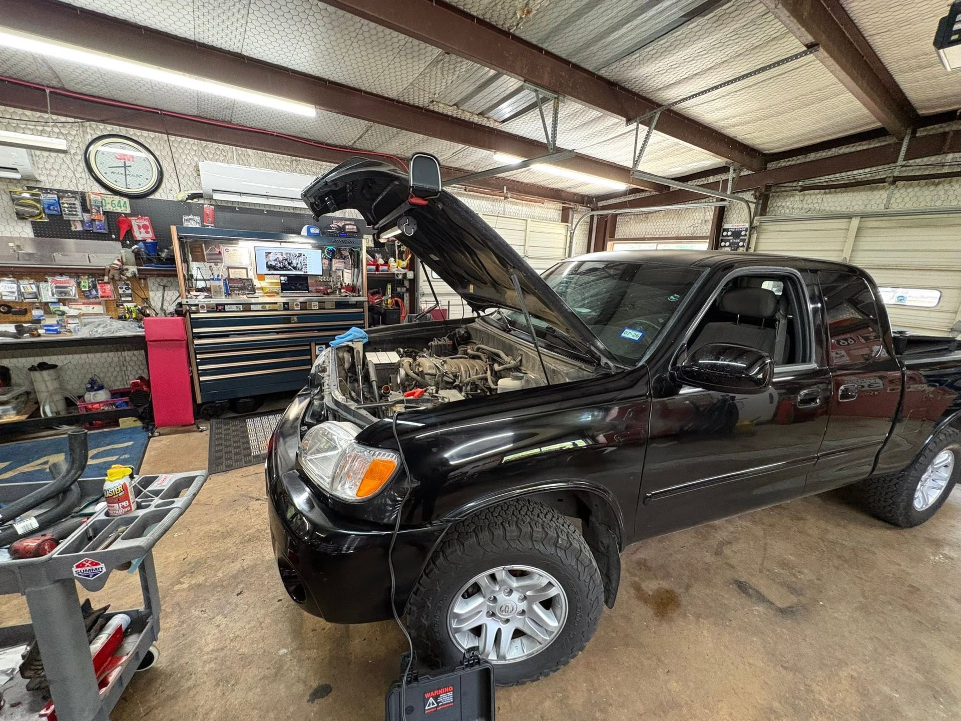 Black pickup truck with hood open inside an auto repair shop