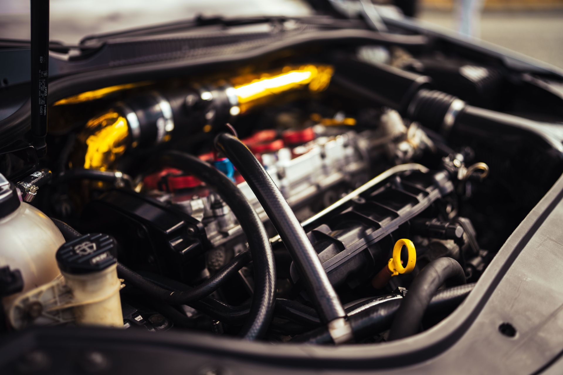 Close-up of a car engine bay with hoses, metal components, and a yellow oil dipstick