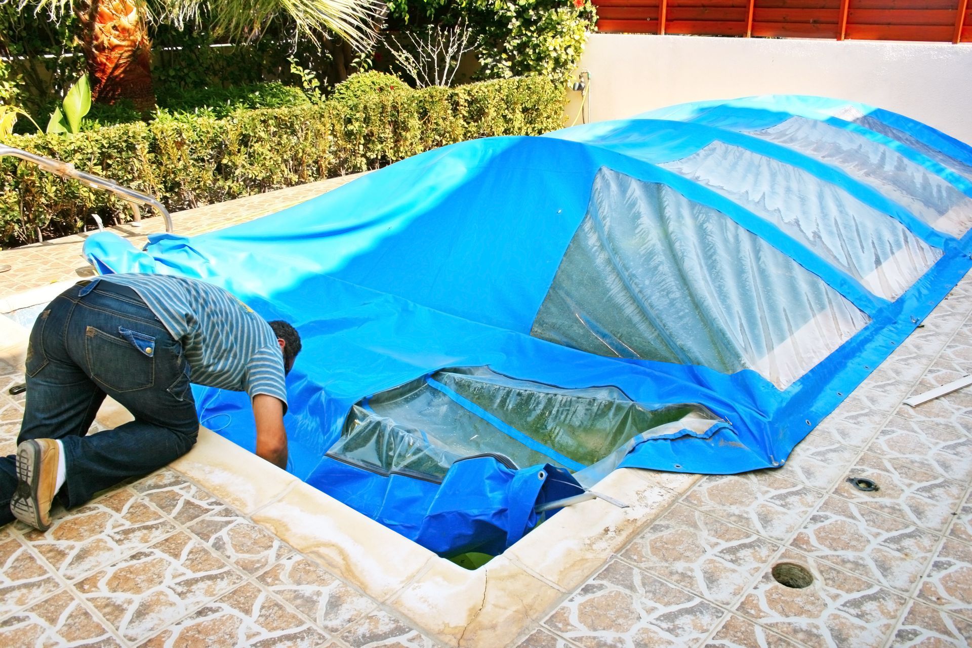 a man snapping on a plastic pool cover over a small pool.