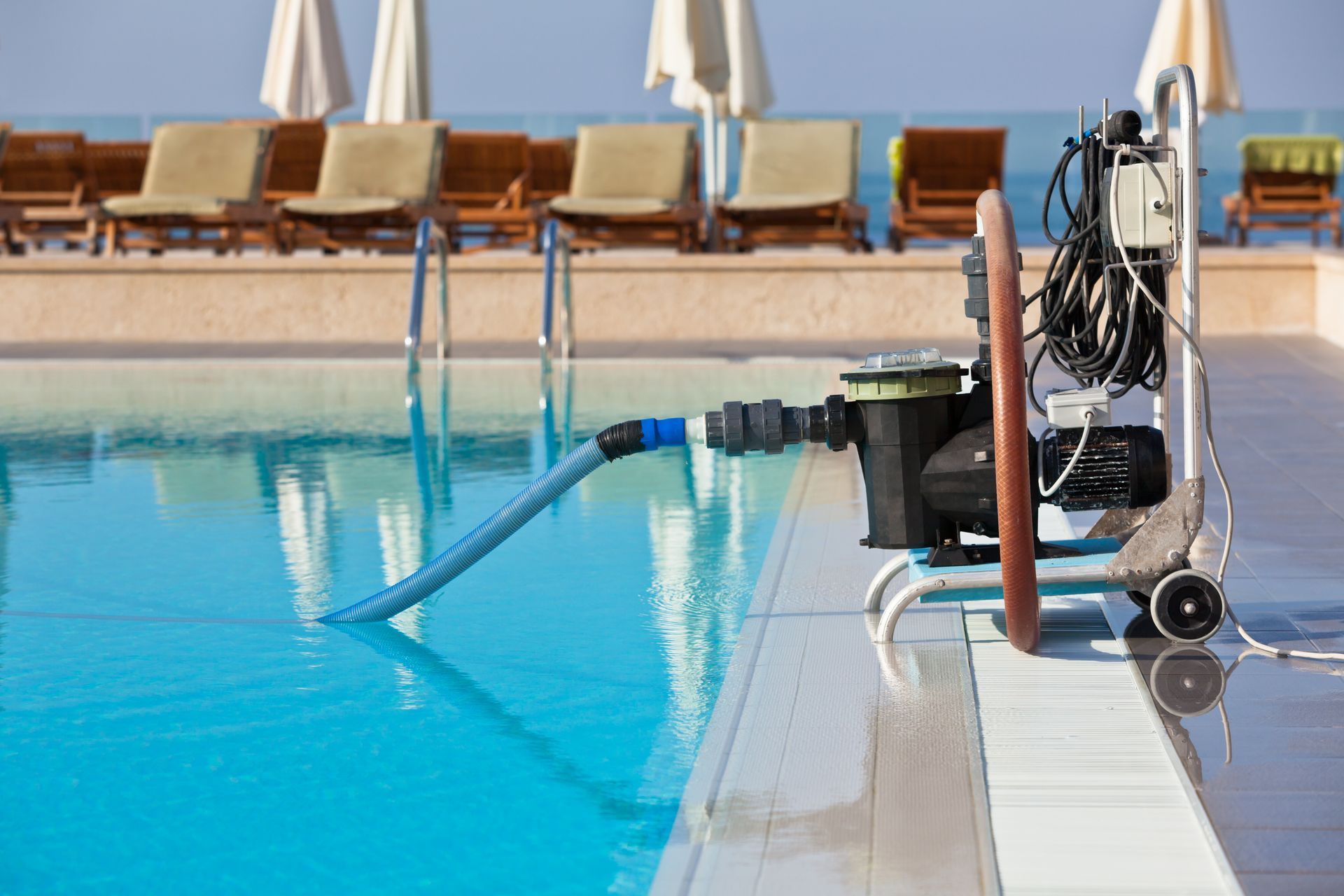 a suction pool cleaner motor on the deck of a pool next to the water with the hose going out into the pool.