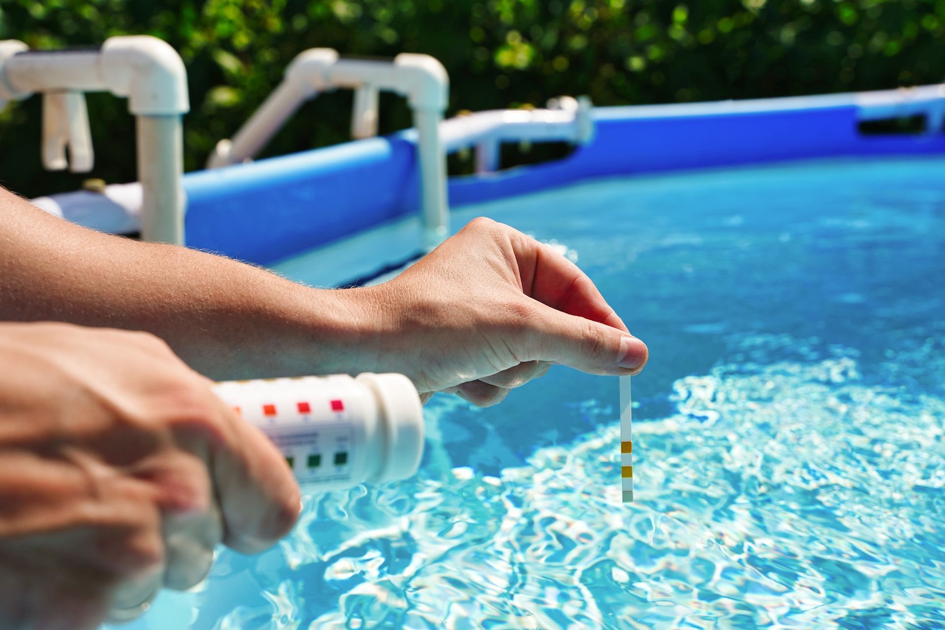 a women's hands dipping a pH testing strip into a small above ground pool.